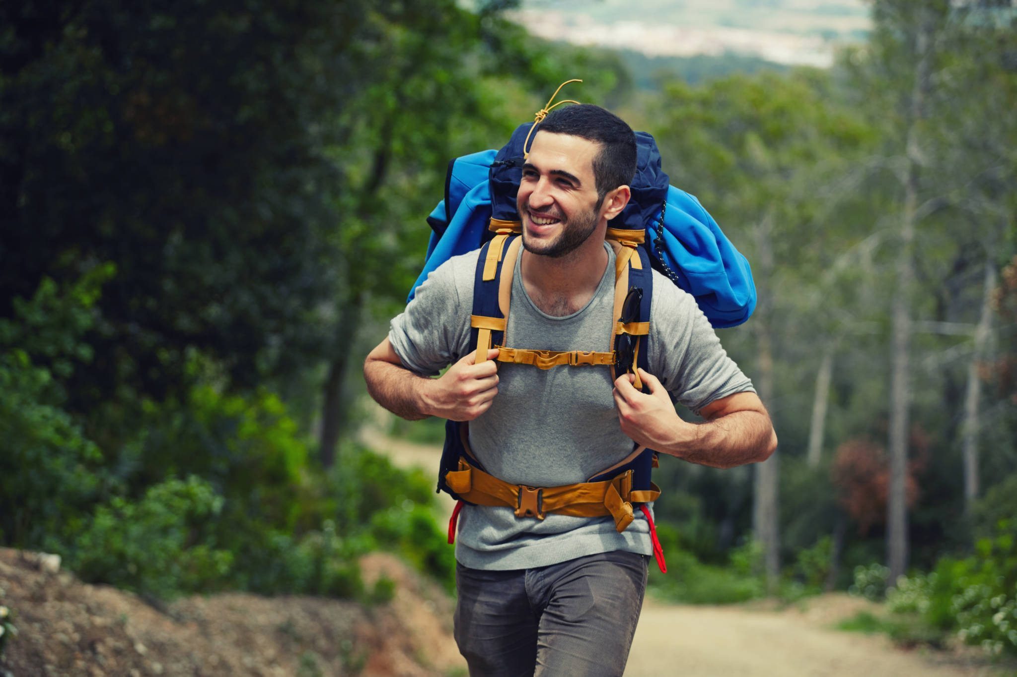 Young hiker with rucksack walking up on the trail and smiling