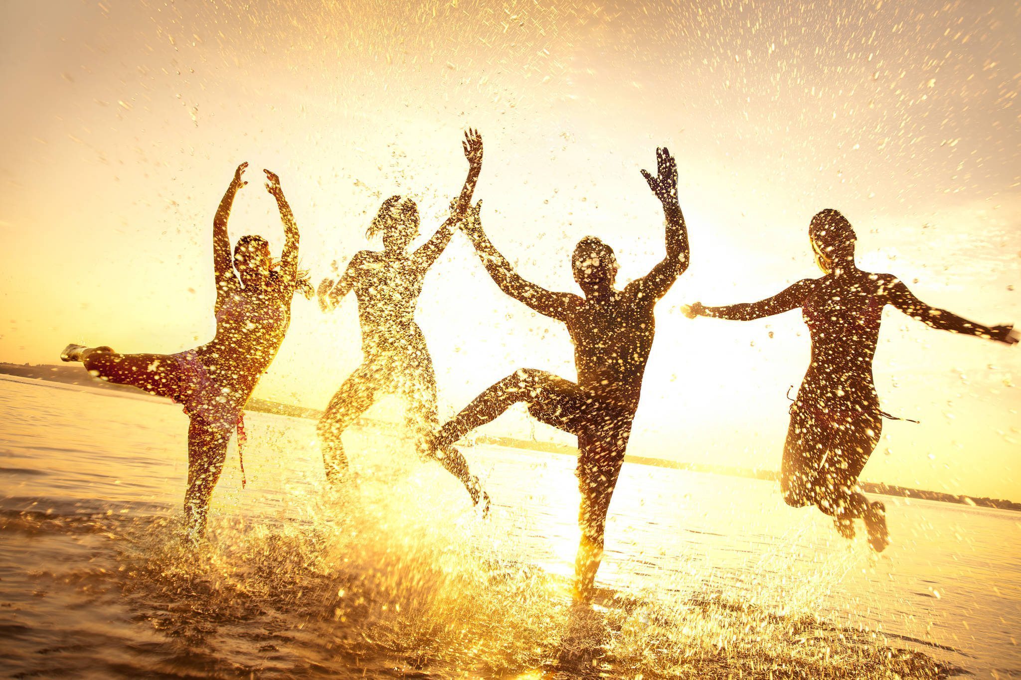 group of happy young people dancing and spraying at the beach on beautiful summer sunset