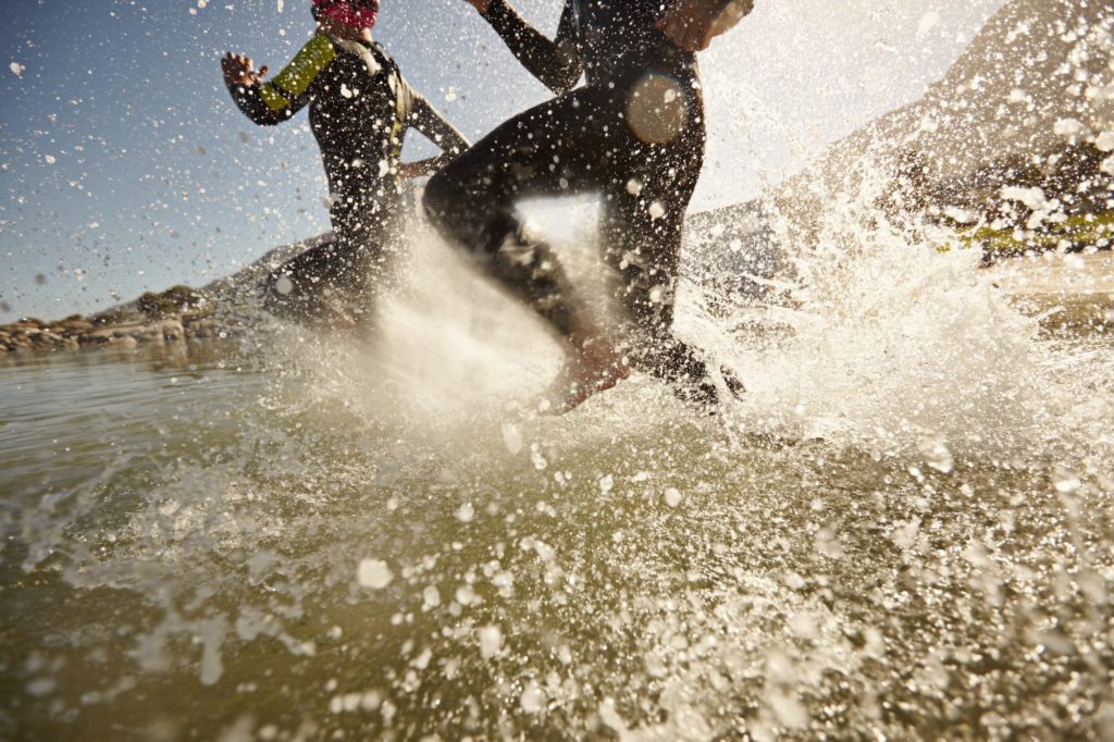 Two triathlon participants running into the water for swim portion of race. 